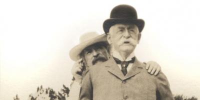 sepia photograph of Mark Twain standing behind Henry H. Rogers in Bermuda, 1908