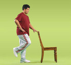 Man checking his balance by standing on one foot while holding onto a chair. - Click to enlarge in new window.