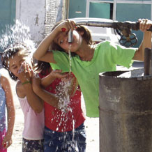 Photograph of kids drinking out of a water pipe.