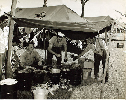 A black and white picture of people standing under a tent