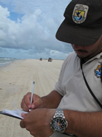 A man wearing a USFWS hat and shirt writes notes on the beach during a NRDAR survey