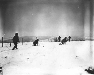 John Perry, a movie photographer with Unit 129, films GIs of the 290th Infantry Regiment, 75th Infantry Division, and 4th Cavalry Group ferreting out German snipers near Beffe, Belgium. Twelve Germans were killed. The scene was photographed by Carmen Corrado of the 129th. January 7, 1945. US Army Signal Corps photograph taken by C.A. Corrado.