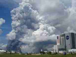 Third Place, W/UI- Photo of Kennedy Space Center, Vehicle Assembly Building (VAB), where space shuttle is assembled. Smoke rising through the cumulous layer during an RX Burn.  Merritt Island National Wildlife Refuge, FL; 2007.