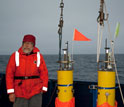 Photo of scientist Eric D'Asaro standing on deck with robotic floats he developed.