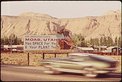 photo by David Hiser large sign of 'Mr. Manufacturer: Moab, Utah has space for you and your plant too' and a car speeding past