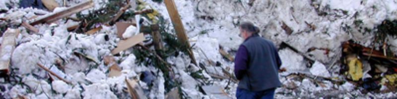 January 30th, 2000. A man looks through rubble covered in snow and ice.