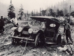 Photo of an old car stuck in a muddy road with three men trying to get it out of the mud