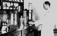 Black and white photo of scientist in lab coat working in a laboratory in the 1880s
