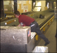 Worker bending over conveyor to get baggage
