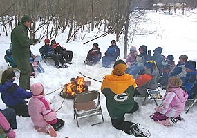 Junior Rangers gather around a campfire (built in a metal garbage can cover) while a Park Ranger weaves a story.