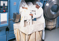 Commericial laundry worker unloading a washing machine into a laundry cart