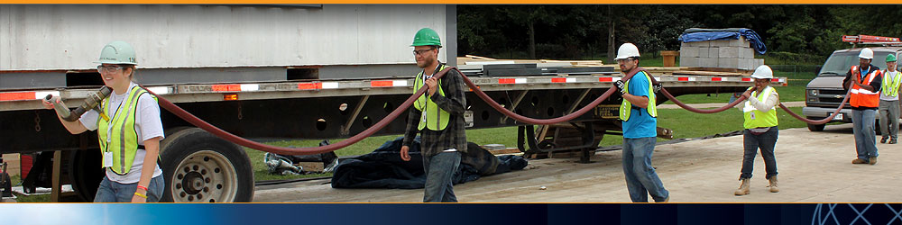 Photo of a line of Solar Decathlon team members in safety gear carrying a long water hose.