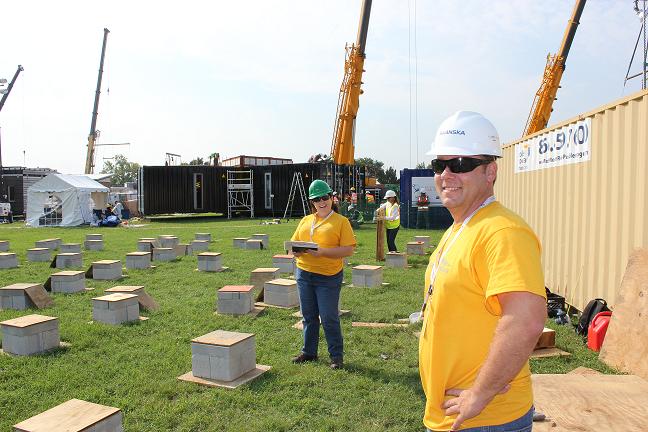 Photo of smiling people standing next to about 30 blocks about a foot square that are spaced along the grass.