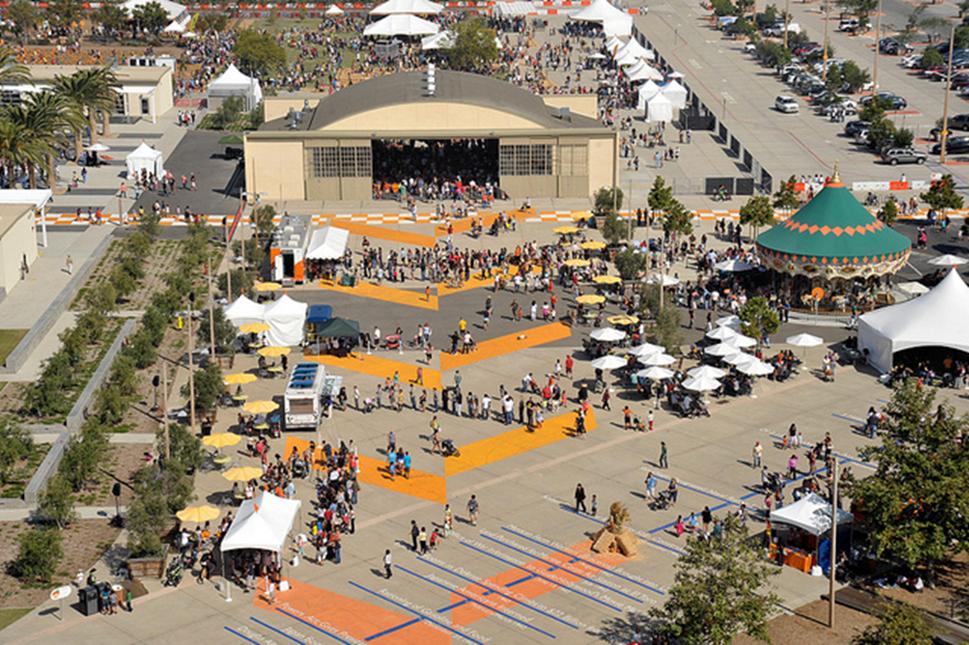 Photo of crowds of people at an outdoor event. In the center is an airplane hangar.