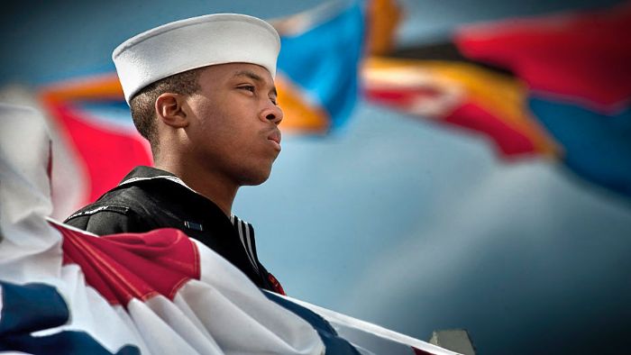 Operations Specialist Seaman mans the rails aboard an Arleigh Burke-class guided-missile destroyer during the ship's commissioning ceremony.