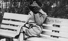 A woman sits on a park bench marked “Only for Jews.” Austria, ca. March 1938.