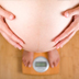 Photo of a pregnant woman on a scale holding her belly.