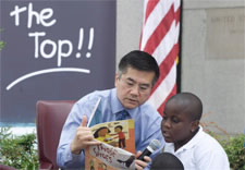 Locke seated and holding book while children look on. Click for larger image.