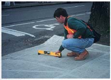 Figure 11-17. The curb ramp slope is being measured for positive slope with a digital inclinometer.