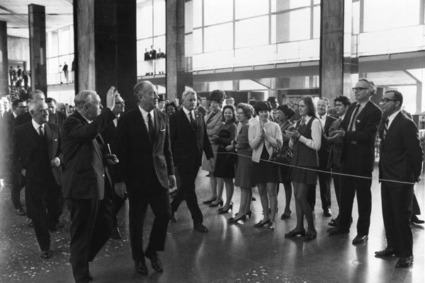 January 27, 1970:  An SY special agent (center, rear) escorts Prime Minister Harold Wilson of Great Britain (waving) and U.S. Secretary of State William P. Rogers in the lobby of the Main State (now Harry S Truman) building at the U.S. Department of State. (Source: Private Collection)