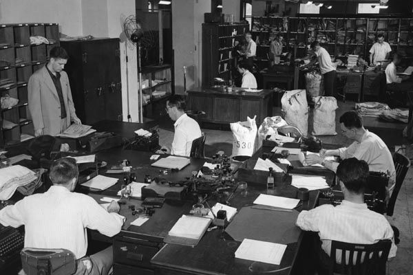 A Diplomatic Courier (left) waits in U.S. State Department mail room in 1948 as diplomatic pouch contents are sorted and logged. (U.S. Department of State photo)