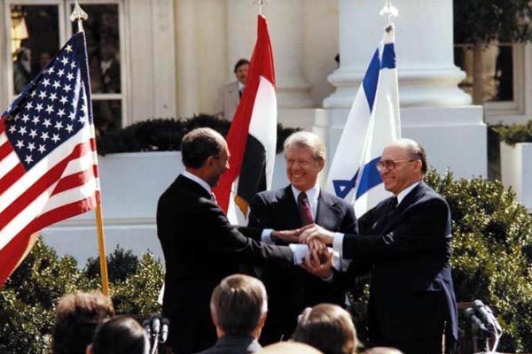 September 17, 1978:  An SY special agent on protective security detail (center rear, behind Egyptian flag) watches as Egyptian President Anwar Sadat, U.S. President Jimmy Carter, and Israeli Prime Minister Menachim Begin celebrate the newly signed Camp David Peace Accord at the White House. (Source:  U.S. Department of State)