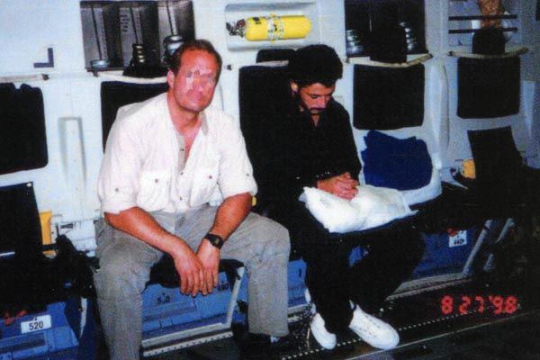 August 27, 1998:  A DS special agent guards terrorist Mohammed Sadiq Odeh onboard a military aircraft as Odeh is brought to justice. DS is part of a U.S.-Kenyan operation to capture those responsible for the bombing of U.S. Embassy Nairobi. Odeh is later convicted in U.S. Federal Court. (Source: Private Collection) 
