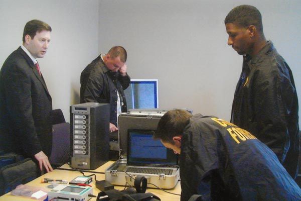 June 17, 2008:  A Computer Investigations and Forensics (CIF) branch chief (left) observes as DS special agents prepare portable equipment used to make forensically valid images of digital evidence in the field. CIF assists in several capacities, including visa and passport fraud, other criminal cases, and counter-intelligence. (Source: U.S. Department of State)