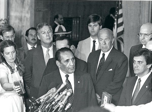 May 20, 1984: SY special agent Mark Moretti  (rear center with black necktie) looks on as President Jose N. Duarte of El Salvador (center) addresses the news media at U.S. State Department headquarters. U.S. Secretary of State George Shultz and Ambassador to El Salvador Thomas Pickering (with glasses) stand slightly behind and to President Duarte's left. (Source: U.S. Department of State)