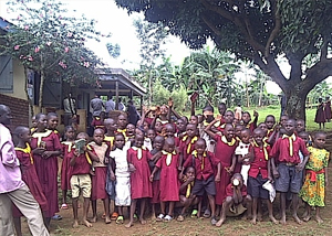 A large group of school children under a tree, smiling fo rthe camera