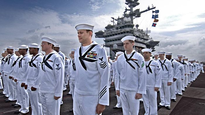 Sailors prepare to man the rails on the flight deck aboard an aircraft carrier.