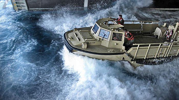 A Construction Mechanic drives a light amphibious re-supply cargo vehicle through the well deck of an amphibious assault ship.