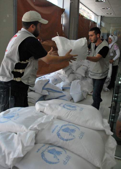 Syrian Red Crescent staff carry sacs of food at a distribution center for internally displaced people in Damascus. 