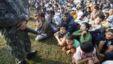 A Thai soldier stands guard as refugees from Burma sit at the Thai-Burma border town of Mae Sot, waiting to go to refugee camps in Thailand, November 9, 2010.