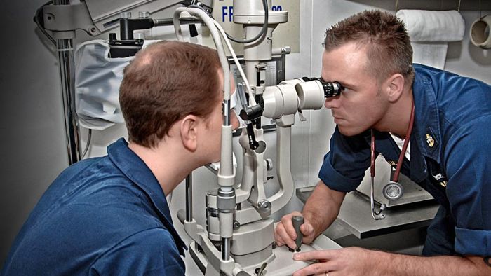 Chief Hospital Corpsman performs an eye exam on a patient aboard an aircraft carrier.