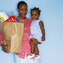 Mother holding a toddler in one arm and a grocery bag in the other.