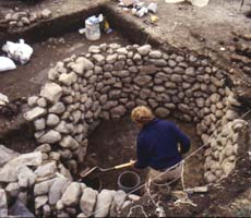 (photo) An archeologist stands inside a rock-lined well. (Massachusetts Historical Commission)