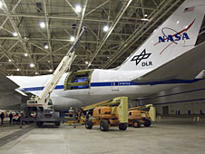 A large mobile crane removing the aperture assembly and cavity doors from NASA's SOFIA observatory aircraft.