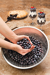 Photo: Hands scooping blueberries out of a bowl with blueberry pie and sundaes in the background. Link to photo information