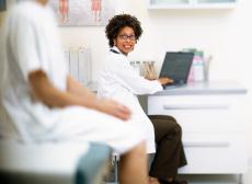 Photograph of a female patient talking to a female doctor using a laptop in an exam room