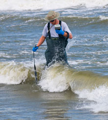 photo of a man walking through 
the surf with water sampling equipment