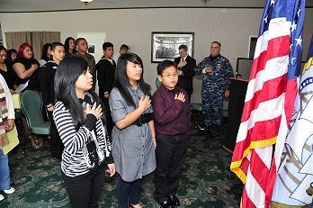 Sisters and brother Chylites, Armina and Arthriel lead the new U.S. citizens in the Pledge of Allegiance during their naturalization ceremony at the Sasebo Naval Station in Japan on Nov. 16, 2010.