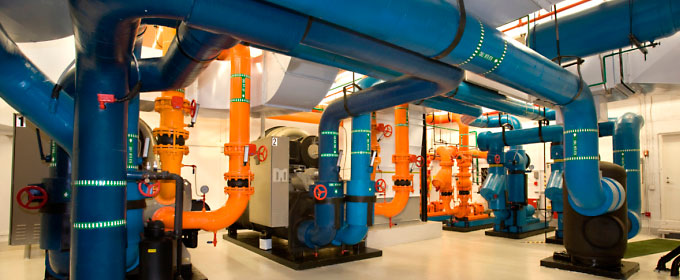 Photo of a factory with a system of large orange and blue pipes snaking throughout.