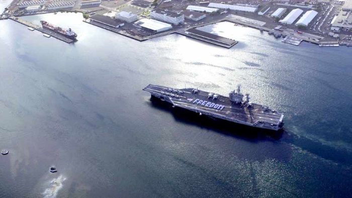 An aircraft carrier passes by the Arizona Memorial as Sailors spell FREEDOM.