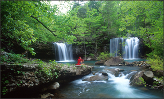 A picture of person that’s enjoying a nearby waterfall that’s flowing into a small creek.