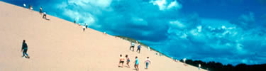 Beneath a blue sky, visitors climb a tall dune at Sleeping Bear Dunes