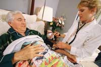 Photo of a nurse assisting an elderly man in a bed.