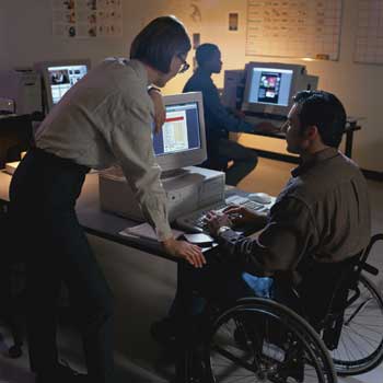 Photo of a teacher helping out a student at his computer.