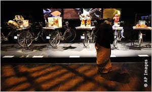 Visitor looking at  bicycles loaded with crafts, with small video screens on rear fenders (AP Images)