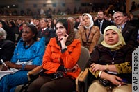 Three women sitting in foreground in large hall, with rows of summit attendees behind (AP Images)